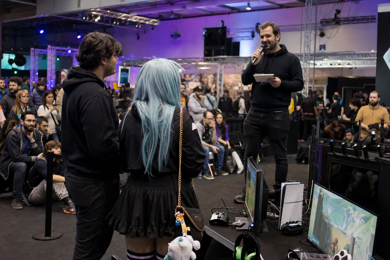 Palco e zona gaming com participantes em competição, público a assistir, júri e prémios em destaque.