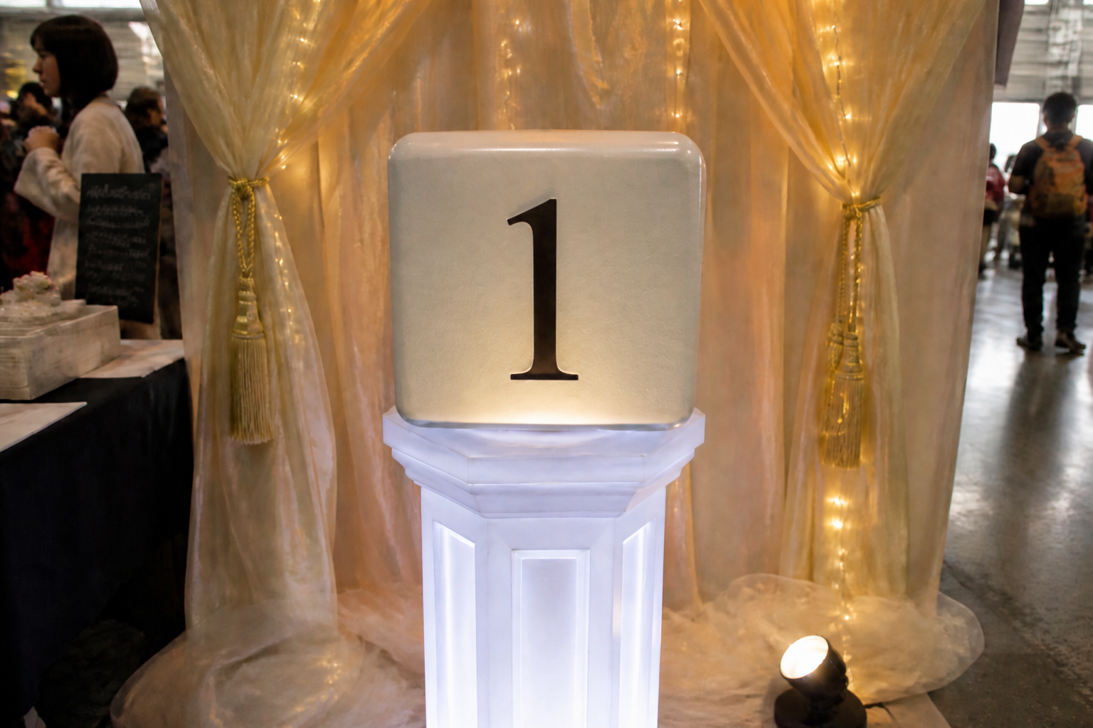 Dado foam grande face 1 em pedestal LED, cortinas champanhe e luzes quentes de palco.